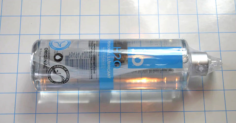 Horizontal view of JO H2O water-based personal lubricant bottle featuring a twist dispenser cap on a grid background