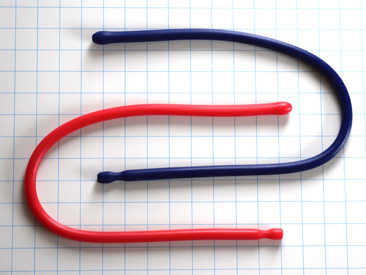 Two 24-inch silicone urethral sounds—one red and one dark blue—curved in a U-shape on a grid background, featuring a 14mm egg-shaped ball tip, 12mm shaft, and retention valley.