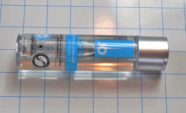 Horizontal view of 4oz JO H2O water-based personal lubricant bottle lying on a grid background.