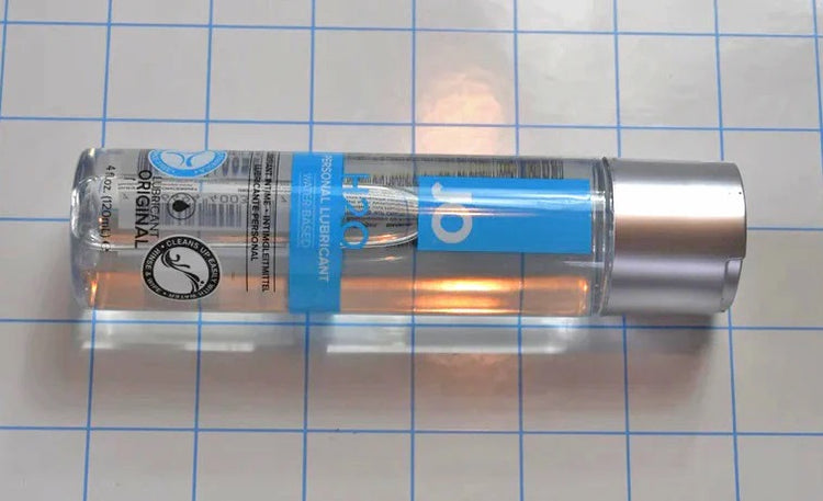 Horizontal view of 4oz JO H2O water-based personal lubricant bottle lying on a grid background.