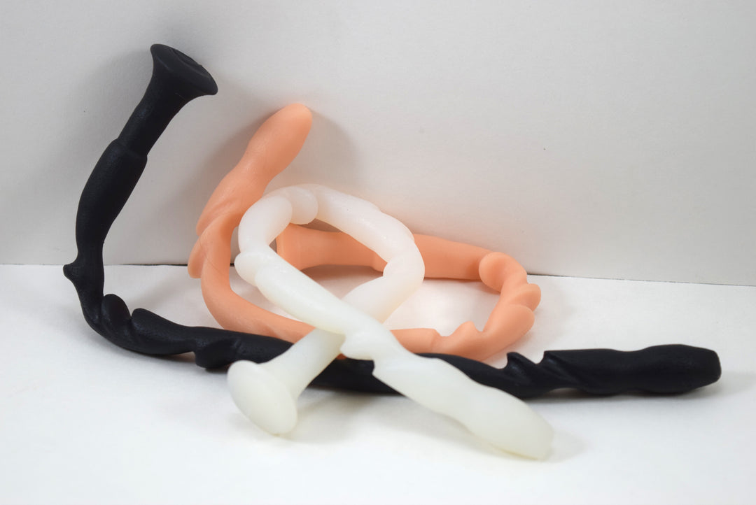 SSND-Totem advanced silicone urethral sounds in black, peach, and translucent white variants shown highly flexed and coiled on a plain white background, highlighting the unique flattened tapered tip and radical alternating 14mm to 15.5mm ridges.