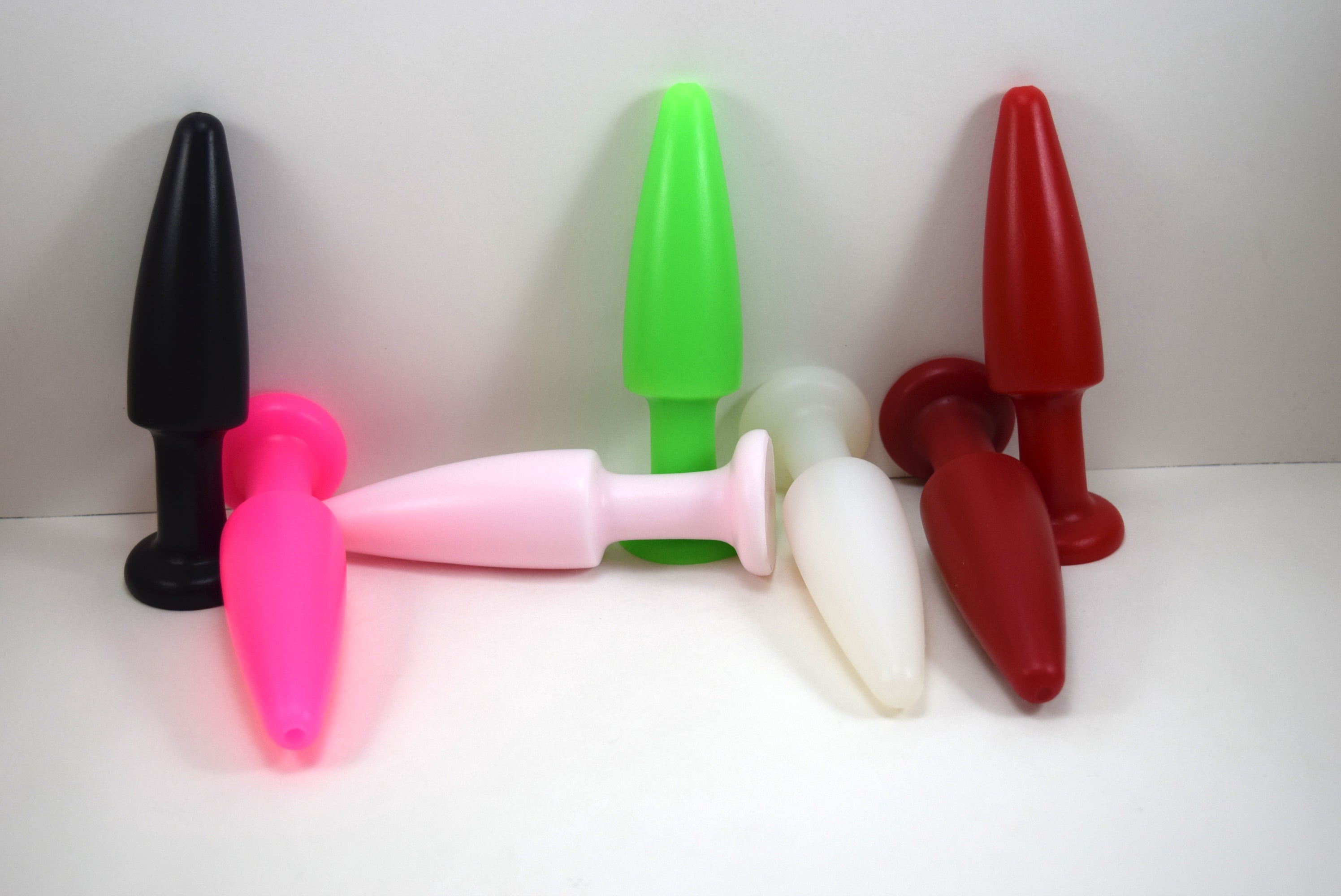 SPD1.5 medium retention style silicone nozzle multi-color lineup featuring black, pink, green, white, and red models with 5-inch tapered tips, 1.5-inch maximum diameters, and safety retention flanges on a blue grid background.