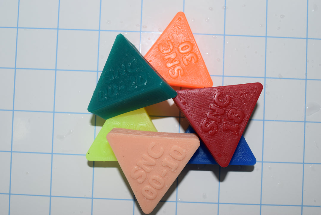 A collection of silicone evaluation triangles in various colors, placed on a checkered background.