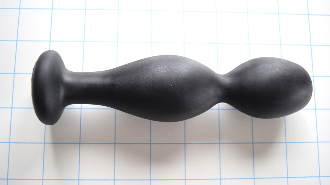 Balltip Medium black silicone enema nozzle featuring a 1.6-inch primary round tip, a 3/4-inch valley, a 1.7-inch secondary expansion bulb, and a wide 1 15/16-inch safety base flange on a blue grid background.
