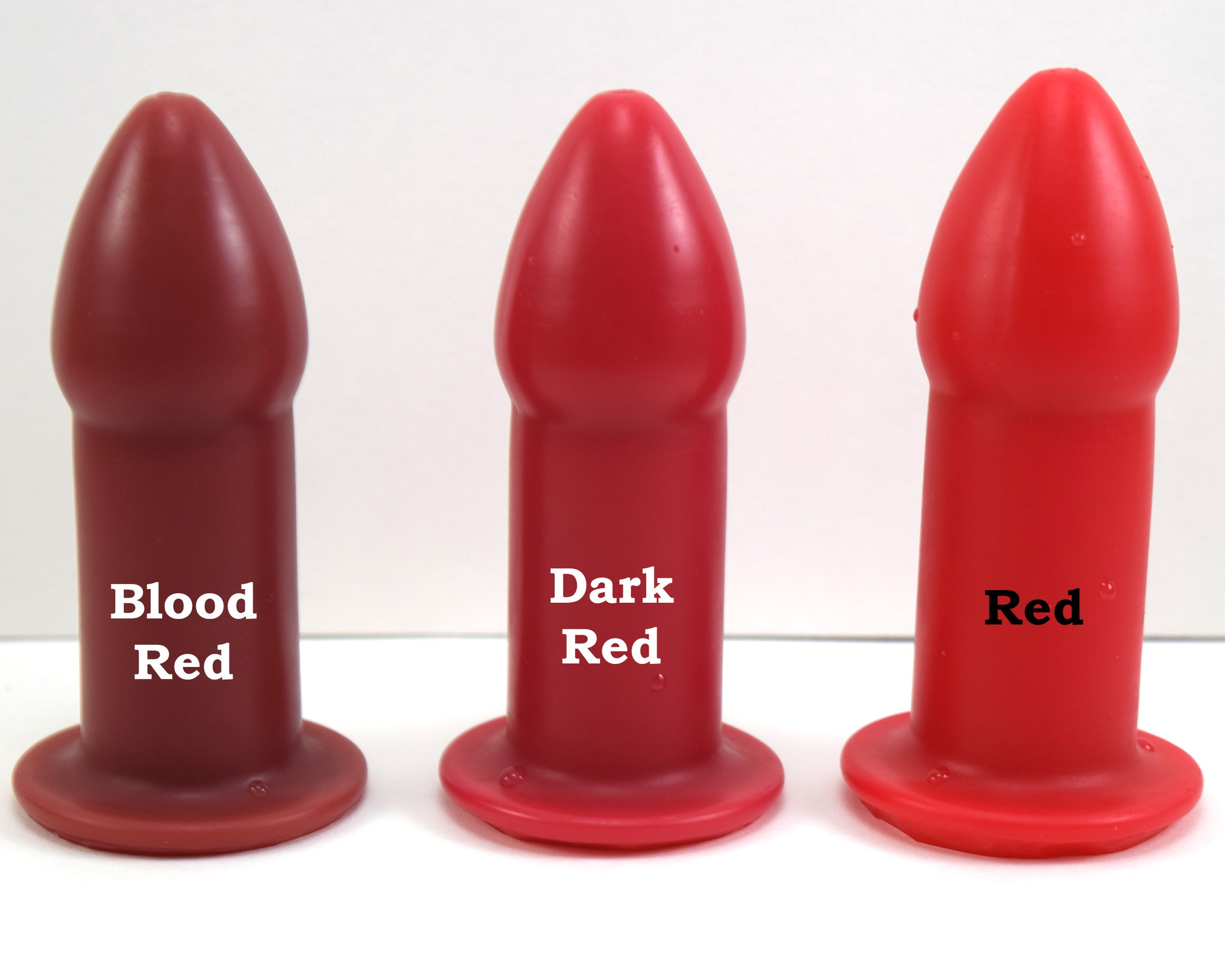Three silicone nozzle plugs displayed side-by-side on a white surface to demonstrate color variations. The plugs are labeled from left to right as 'Blood Red', 'Dark Red', and 'Red'; each features a tapered tip and a wide safety flange