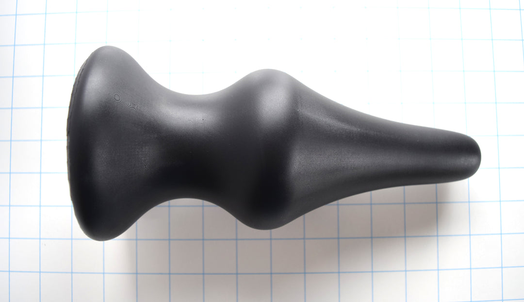 4 inch black silicone Concave SPD plug with long tapered tip and retention valley on a grid background