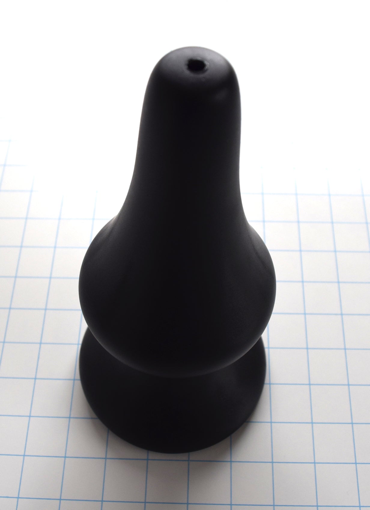4 inch black silicone Concave SPD plug with long tapered tip and retention valley on a grid background standing with tip up