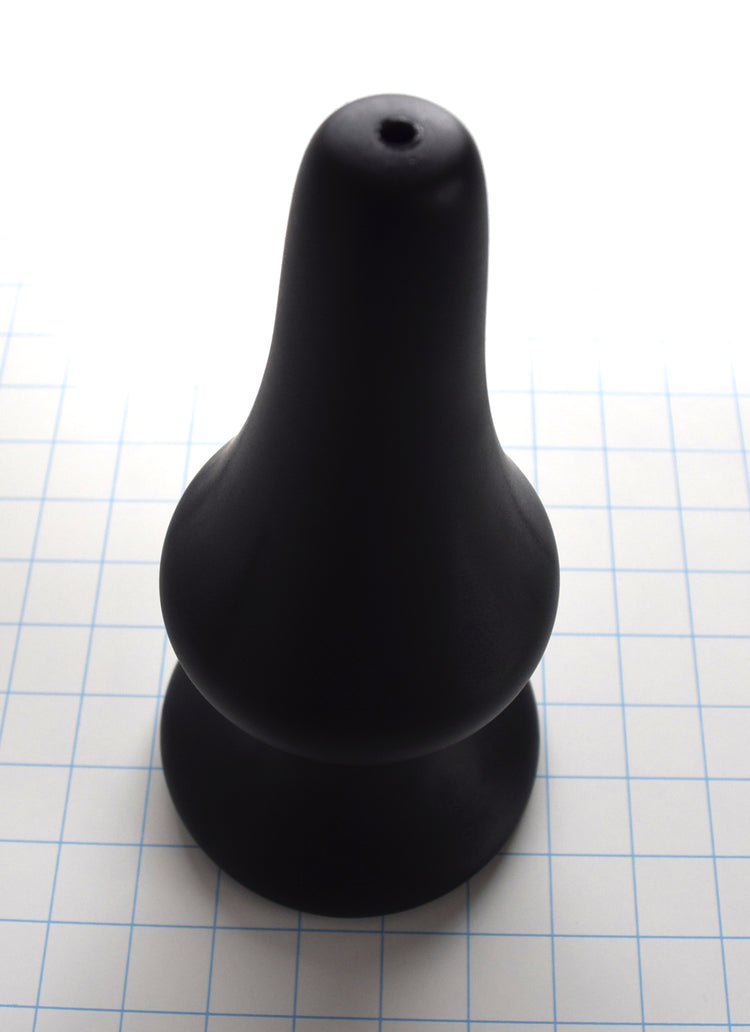 4 inch black silicone Concave SPD plug with long tapered tip and retention valley on a grid background standing with tip up
