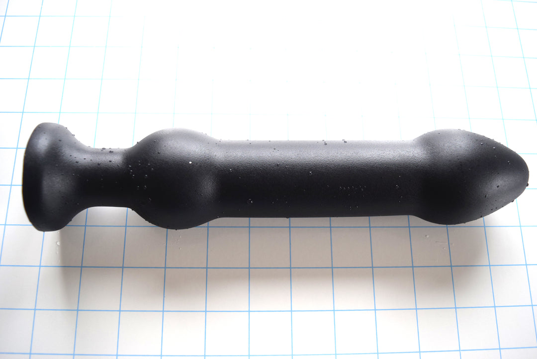 DBLBL 2XL black silicone colon nozzle showcasing its substantial 2.25-inch bulbous tip, thick 1.7-inch central shaft, 2.25-inch secondary retention ball, and flared safety flange base on a grid background