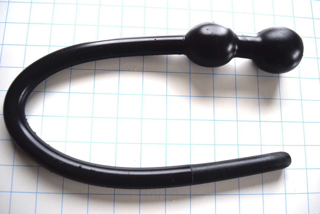 Black silicone U-shaped 3/4-inch deep throat training tube with dual retaining balls on a light blue grid background