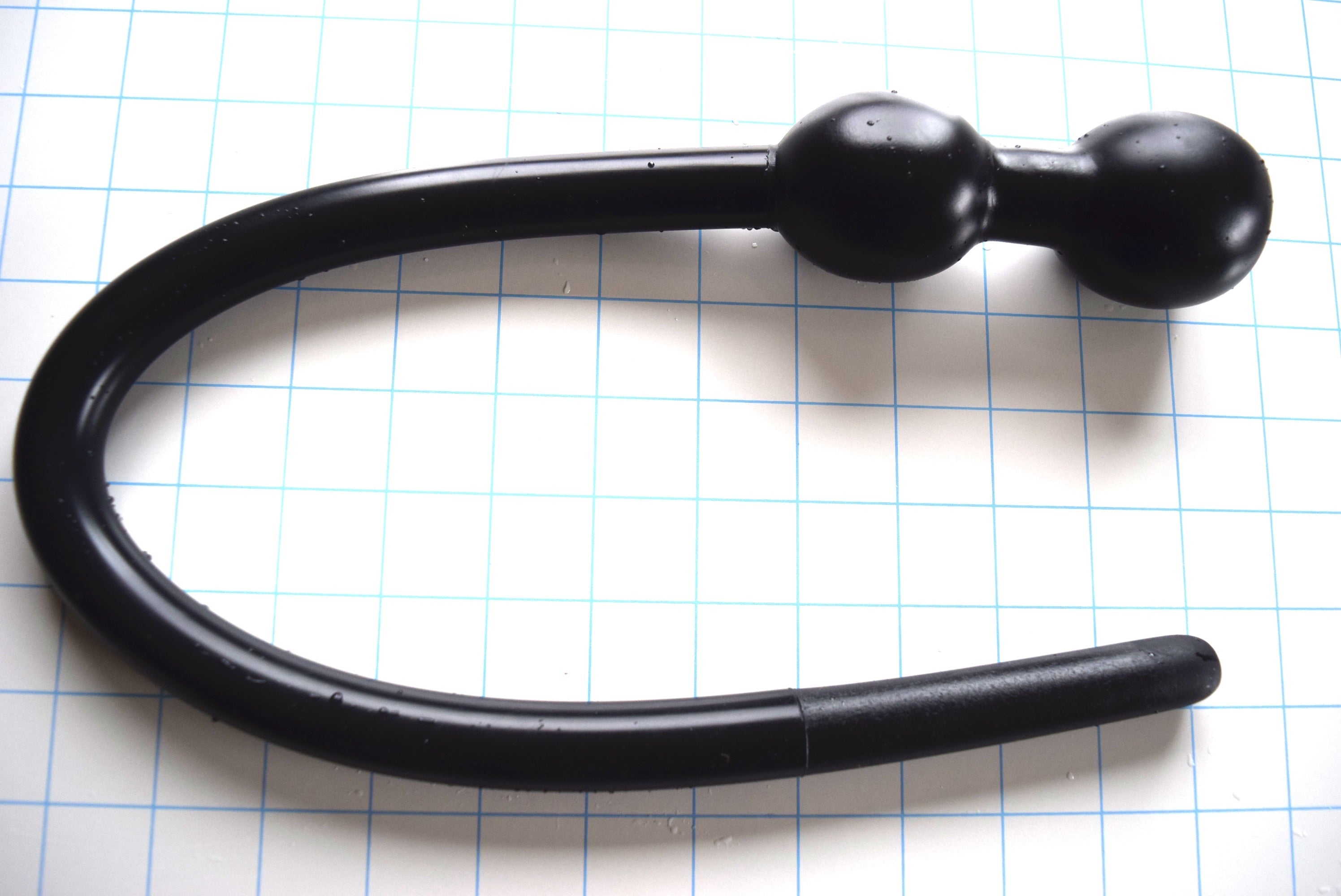Black silicone U-shaped 3/4-inch deep throat training tube with dual retaining balls on a light blue grid background