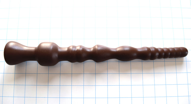 DMD 13-inch chocolate brown silicone enema nozzle on a blue grid background, showcasing its 12 sensory ribs and ridges, a 1.9-inch terminal retention ball, and a deep V-shaped base flange