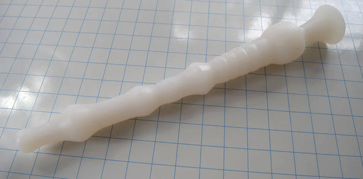 A white multi-dimensional flexible silicone enema nozzle with a ribbed design, shown on a grid background.