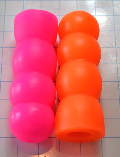 ED-ESS 1 enhancement sleeves displayed side-by-side in pink and orange color variants, showcasing different multi-textured core designs and surface geometries on a grid background.