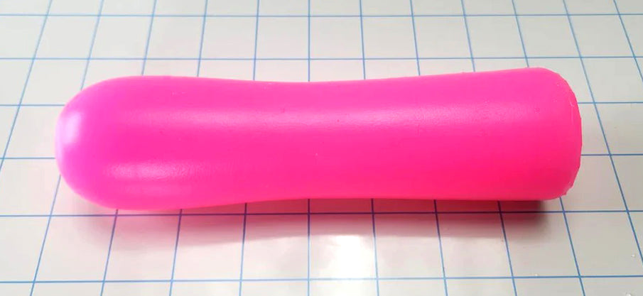 A bright pink, elongated, silky smooth ED-ESS 3 stimulation sleeve placed on a grid paper background, showcasing its smooth exterior and tapered design.