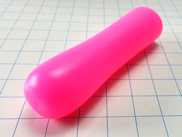 A bright pink, elongated, silky smooth [ED-ESS 3] stimulation sleeve placed on a grid paper background, showcasing its smooth exterior and tapered design.