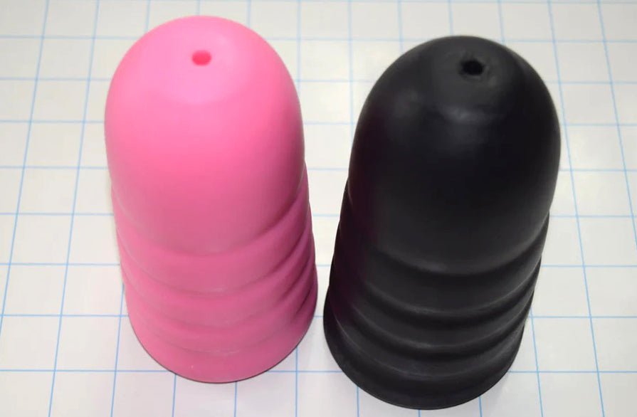 Two artillery shell style ED-ESS 5 stimulation sleeves in pink and black, showing external grip valleys and tapered tips on a grid background.