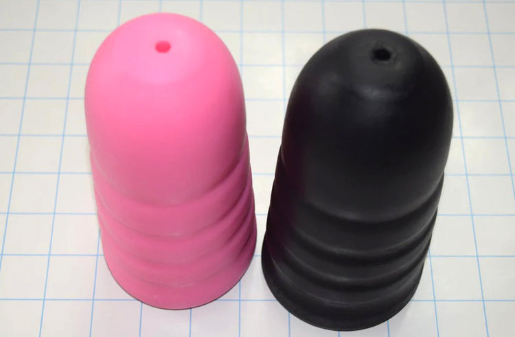 Two artillery shell style ED-ESS 5 stimulation sleeves in pink and black, showing external grip valleys and tapered tips on a grid background.