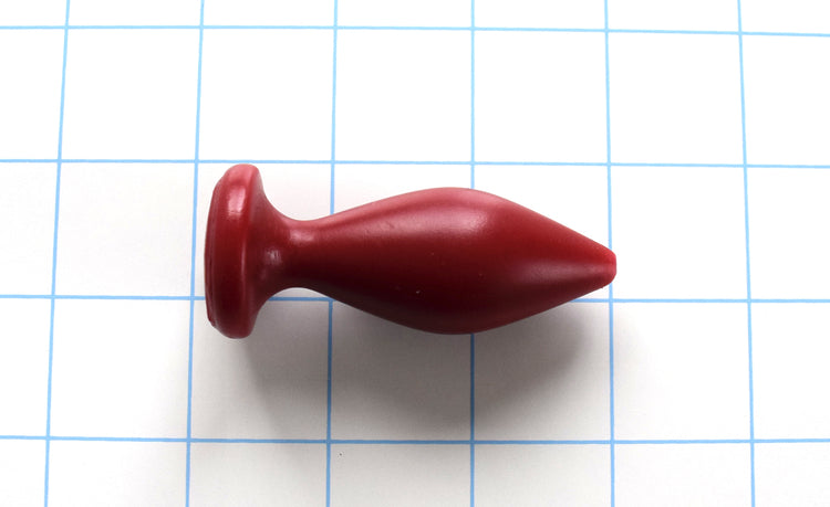 Expanded Diamond 1-inch red silicone retention nozzle featuring a wide faceted diamond body, 2-inch insertable length, ultra-slim retention valley, and flat safety flange on a grid background.
