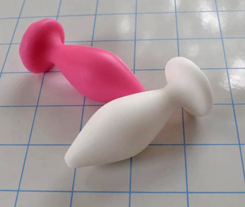 Pair of Expanded Diamond 1-inch silicone retention nozzles in white and pink showcasing their wide faceted diamond bodies, 2-inch insertable lengths, ultra-slim retention valleys, and flat safety flanges on a grid background.