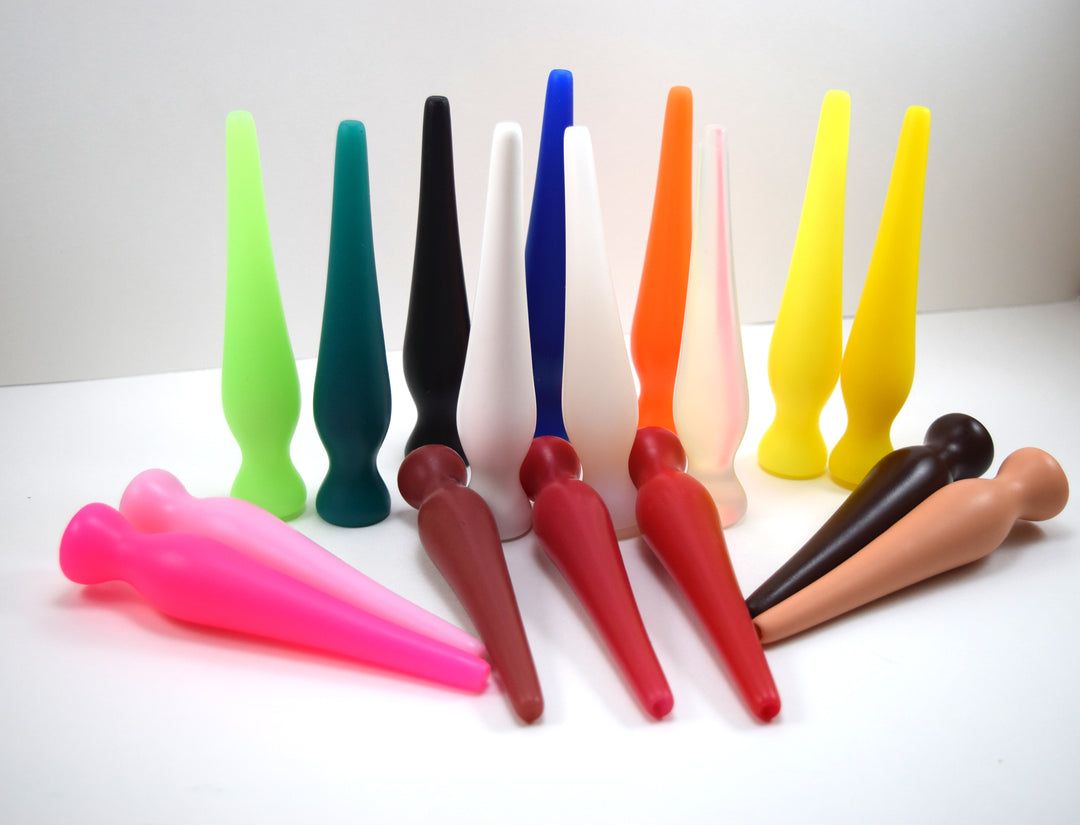 Multiple colorful EXT CON 1.0 inch silicone enema retention plugs displayed together in various material finishes.