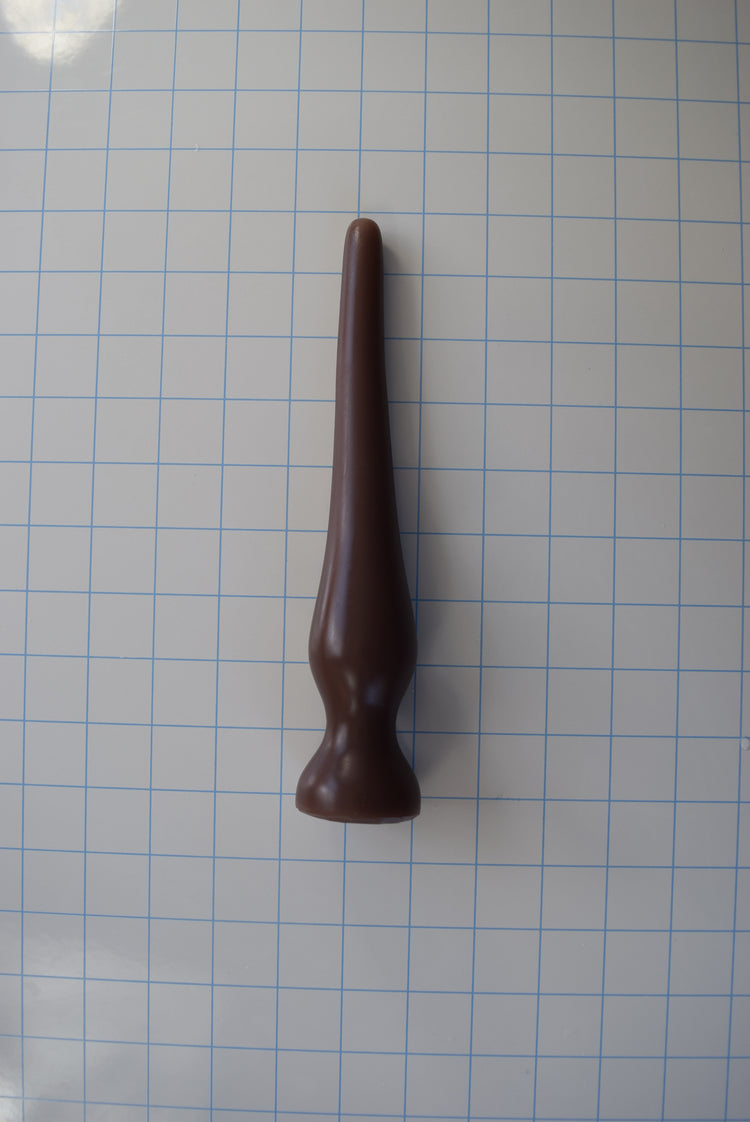 Brown EXT CON 1.5 inch silicone enema plug resting vertically on a blue grid measurement background.