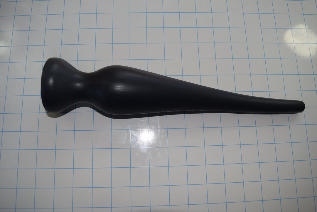 Black EXT CON 2.5 inch silicone enema retention plug lying horizontally on a blue measurement grid facing left.