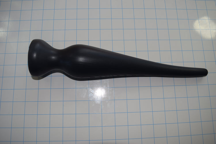 Black EXT CON 2.5 inch silicone enema retention plug lying horizontally on a blue measurement grid facing left.