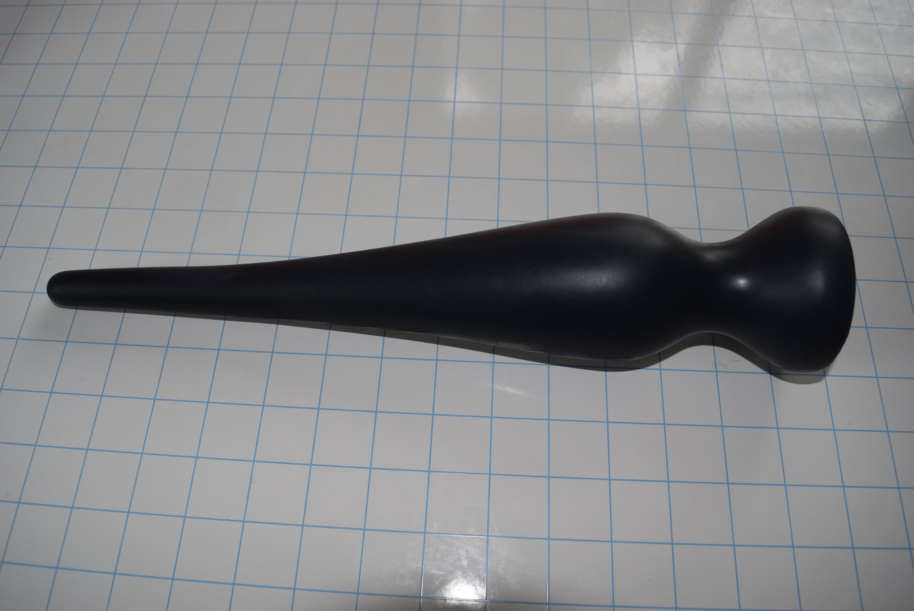Black EXT CON 2.5 inch silicone retention nozzle resting horizontally across a blue measurement grid facing right.