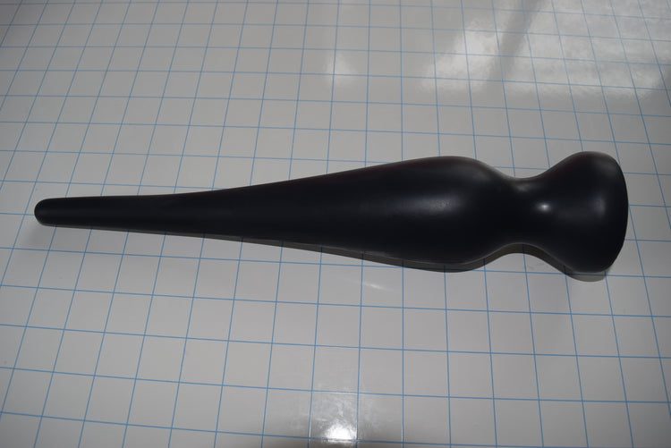 Black EXT CON 2.5 inch silicone retention nozzle resting horizontally across a blue measurement grid facing right.