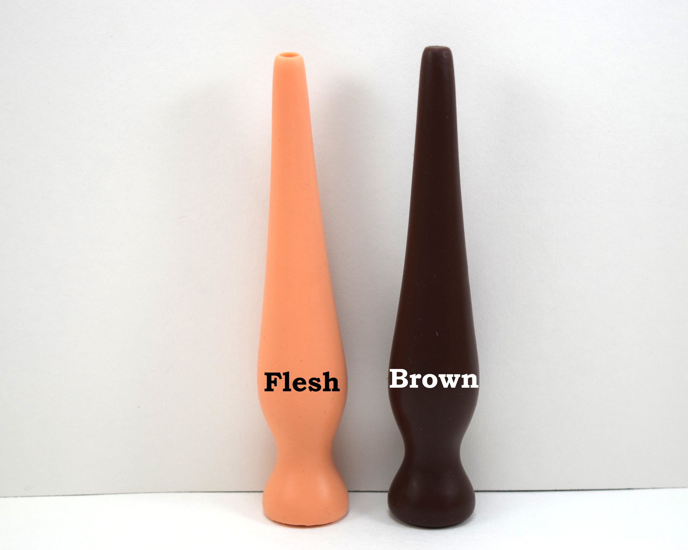 Two long silicone nozzle plugs displayed side-by-side on a white surface to demonstrate color differences. The plugs are labeled from left to right as 'Flesh' and 'Brown'; each features an elongated, tapered shape with a rounded base
