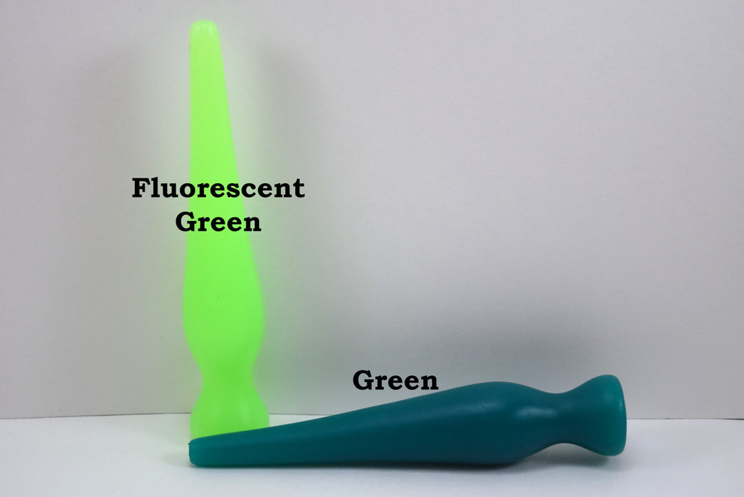Two long silicone nozzle plugs shown against a white background to illustrate color differences. The plug standing vertically is labeled 'Fluorescent Green', and the plug lying horizontally is labeled 'Green'; both feature an elongated, tapered shape