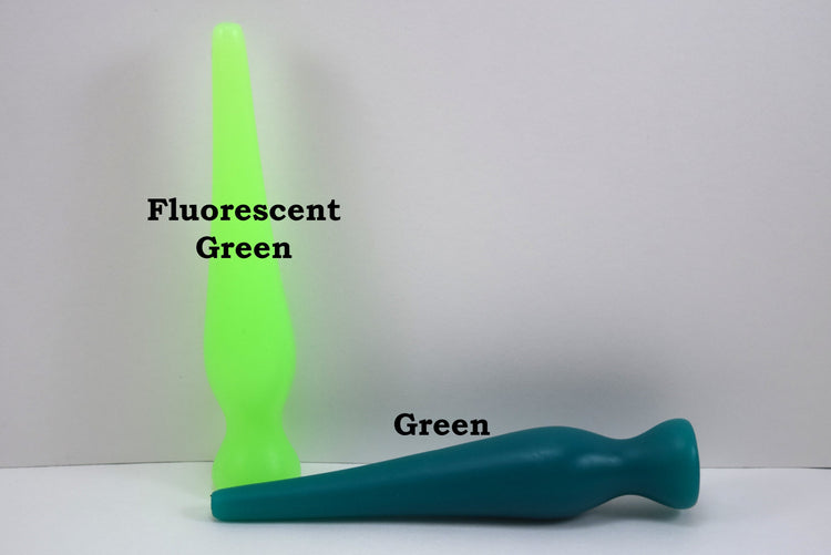 Two long silicone nozzle plugs shown against a white background to illustrate color differences. The plug standing vertically is labeled 'Fluorescent Green', and the plug lying horizontally is labeled 'Green'; both feature an elongated, tapered shape