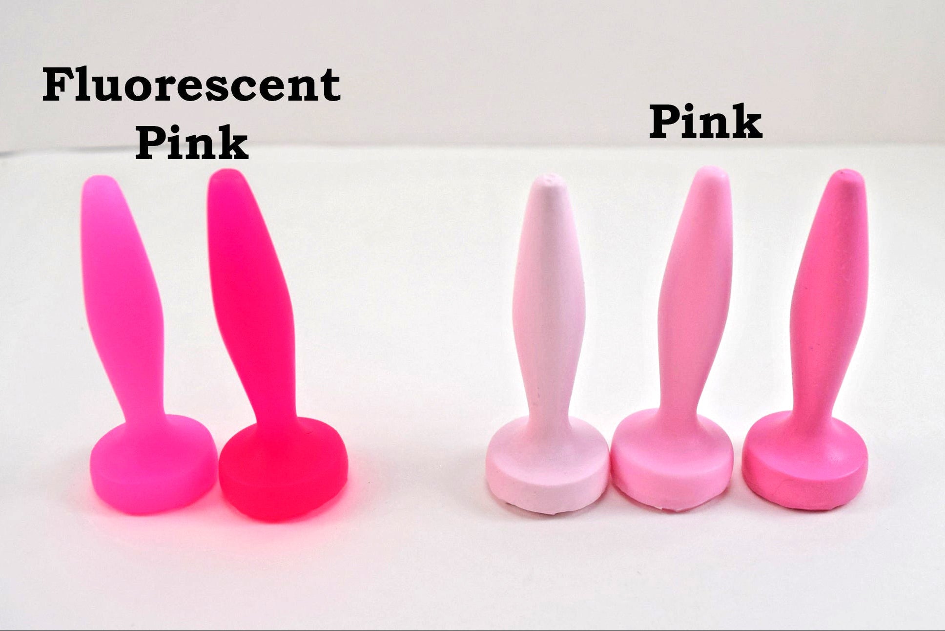 A collection of silicone urethral sounds shown on a white surface to illustrate color variations. The two items on the left are labeled 'Fluorescent Pink', and the three items on the right are labeled 'Pink'; all feature a diamond-shaped body, tapered tip, and flat base