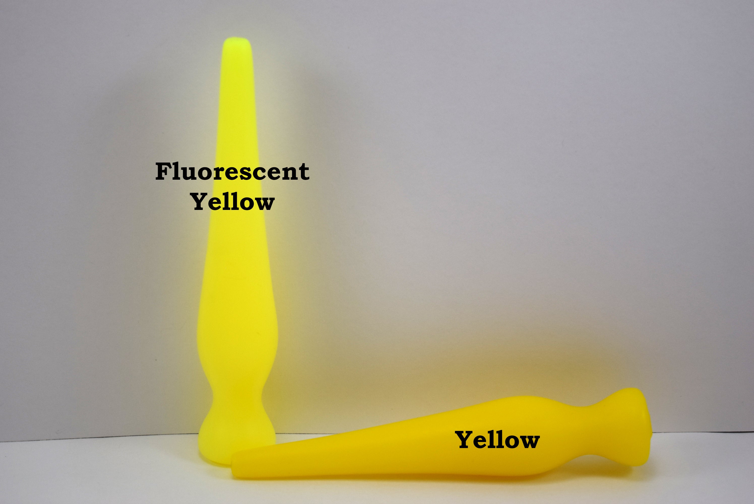 Two long silicone nozzle plugs shown against a white background to illustrate color differences. The plug standing vertically is labeled 'Fluorescent Yellow', and the plug lying horizontally is labeled 'Yellow'; both feature an elongated, tapered shape.