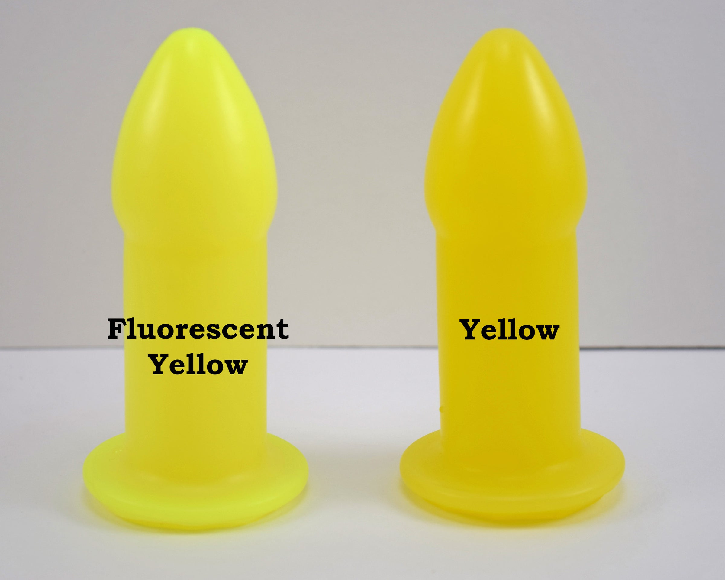 Two silicone nozzle plugs side-by-side on a white surface, demonstrating color differences. The plug on the left is labeled 'Fluorescent Yellow', and the plug on the right is labeled 'Yellow'; both have a tapered tip and wide safety flange