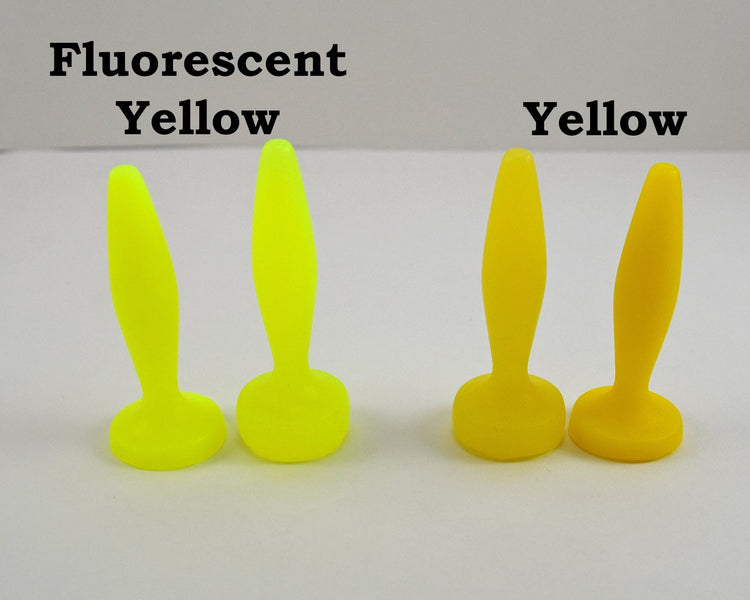Two pairs of silicone urethral sounds displayed on a white surface to show color differences. The pair on the left is labeled 'Fluorescent Yellow', and the pair on the right is labeled 'Yellow'; all feature a diamond-shaped body, tapered tip, and flat base