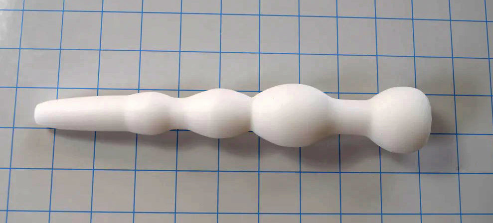 White GRB 36 silicone colon nozzle lying horizontally across a blue measurement grid.