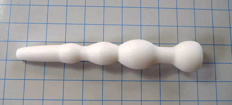 White GRB 36 silicone colon nozzle lying horizontally across a blue measurement grid.