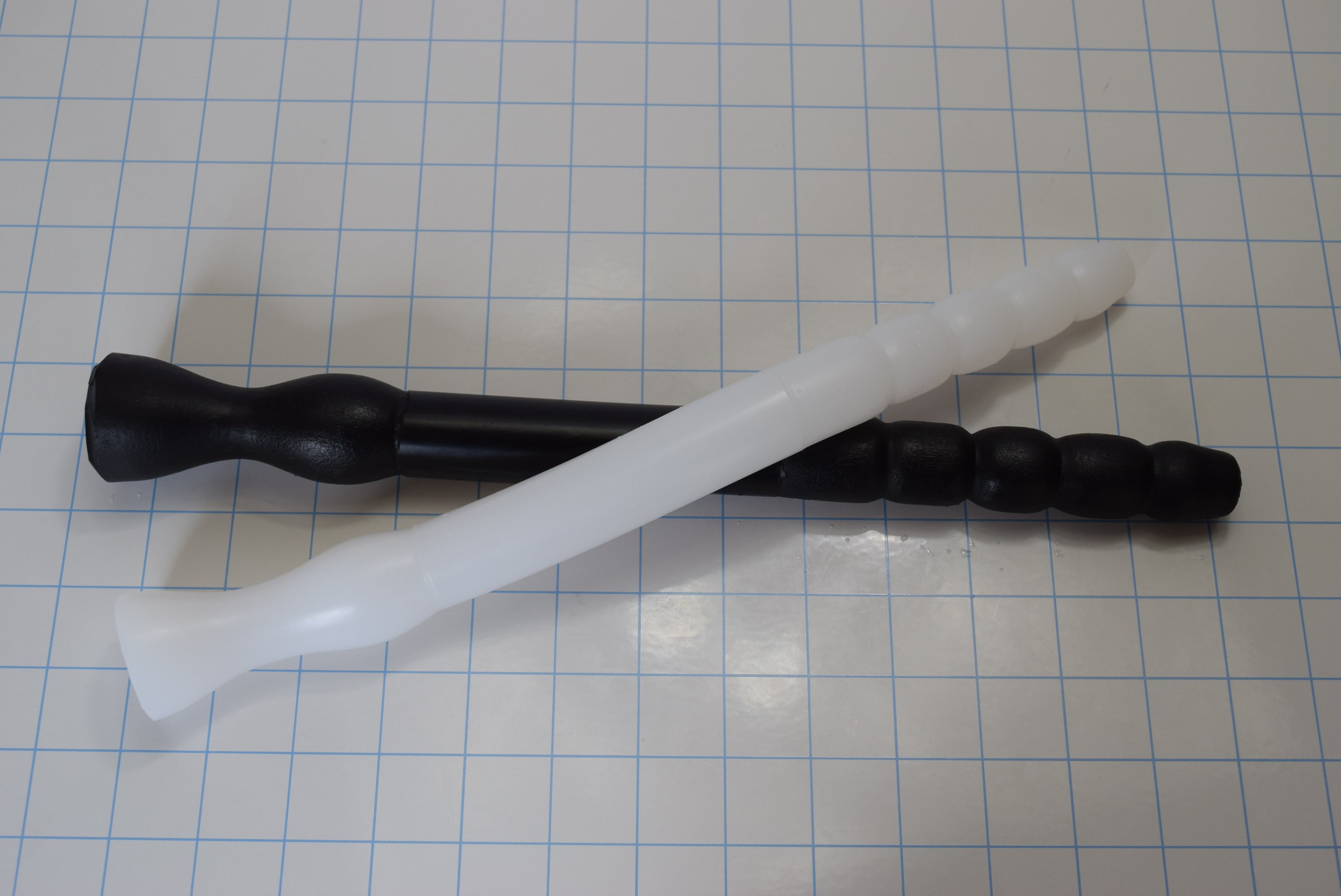 White and black GRB 75 flexible silicone colon tubes crossed over each other on a measurement grid demonstrating tip profiles.