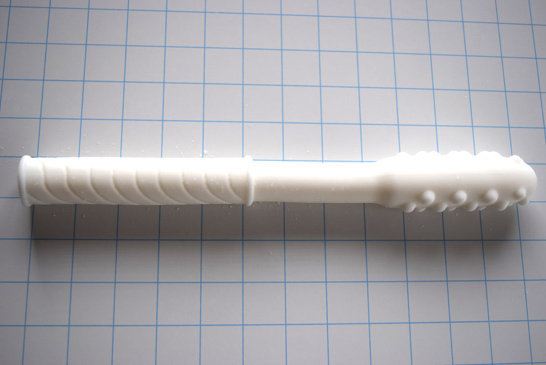 White Knobby Tip silicone enema nozzle with textured bumps and diagonal grip shaft lying horizontally on a blue measurement grid.