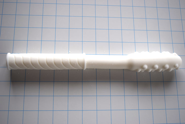 White Knobby Tip silicone enema nozzle with textured bumps and diagonal grip shaft lying horizontally on a blue measurement grid.