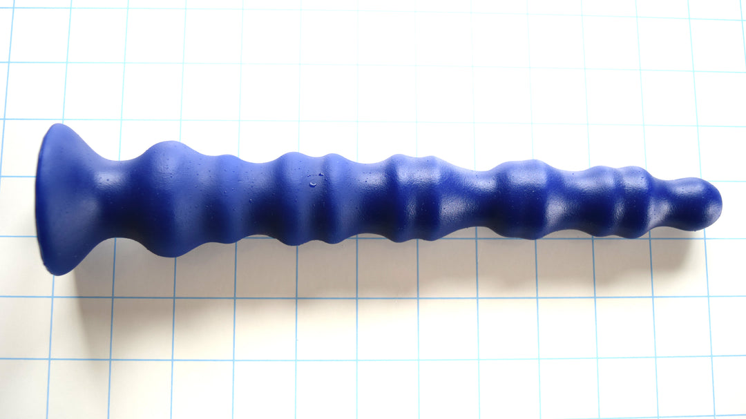 Knuckle 10.5-inch enhanced rib-style colon nozzle in royal blue silicone on a blue grid background, highlighting its five dual-groove knuckle segments and wide flared safety base