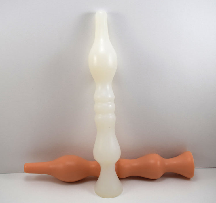 Model B silicone colon tubes shown in vertical translucent-white and horizontal flesh-tone finishes, highlighting the 2-inch guide tip, 1.875-inch egg-shaped bulb, triple modulated mid-ribs, and tapered safety flange