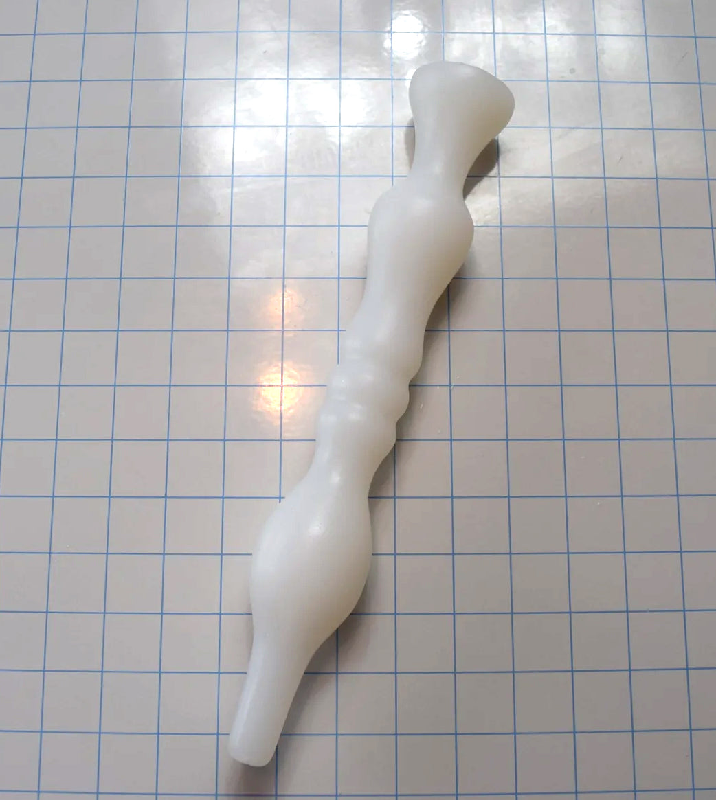 Translucent white Model B silicone enema nozzle with dual sealing bulbs resting diagonally across a blue grid.