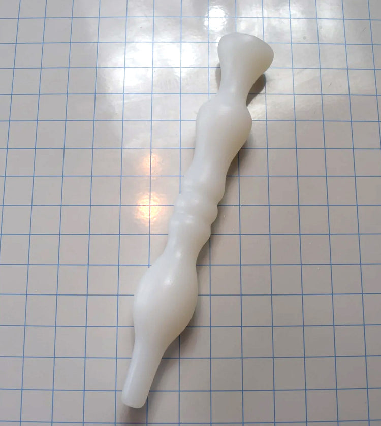 Translucent white Model B silicone enema nozzle with dual sealing bulbs resting diagonally across a blue grid.