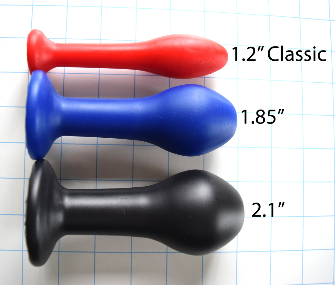 Model M silicone enema nozzles shown in three progressive sizes on a grid: red 1.2-inch Classic, blue 1.85-inch intermediate, and black 2.1-inch advanced model, highlighting their tapered shafts and flared base flanges