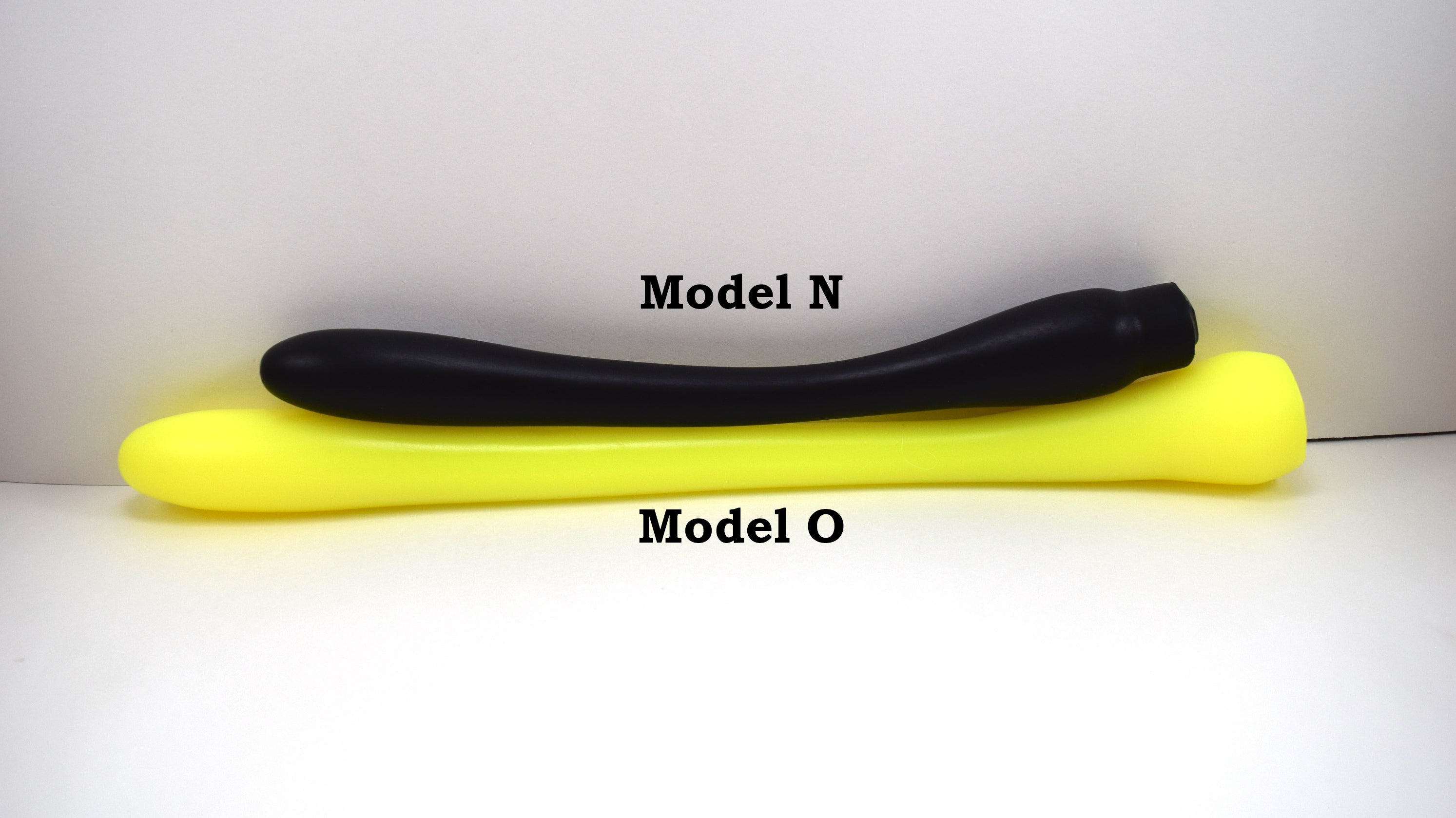 Black Model N silicone enema nozzle lying parallel to a longer yellow Model O nozzle on a white background.