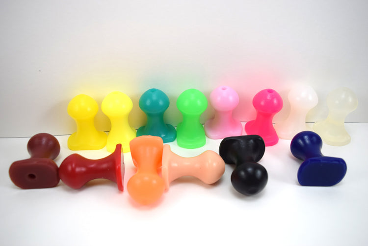 Lineup of multiple Nubby OF silicone retention plugs in various colors featuring 30mm bulbous ball tips, 17mm retention necks, 53mm overall lengths, and ergonomic oval safety flanges on a blue grid background.