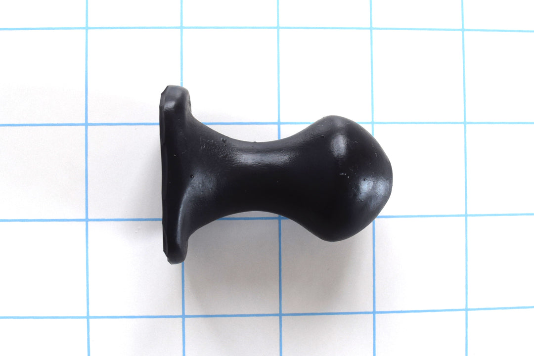 Nubby OF short black silicone retention plug with a bulbous tip and an oval safety flange on a blue grid background